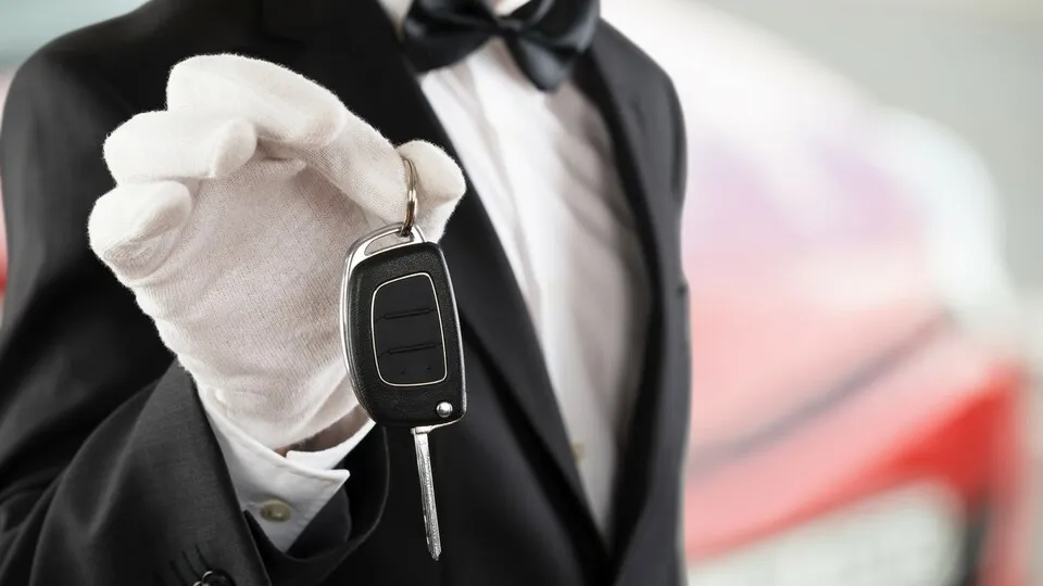 Chauffeur mit weißen Handschuhen vor rotem Auto